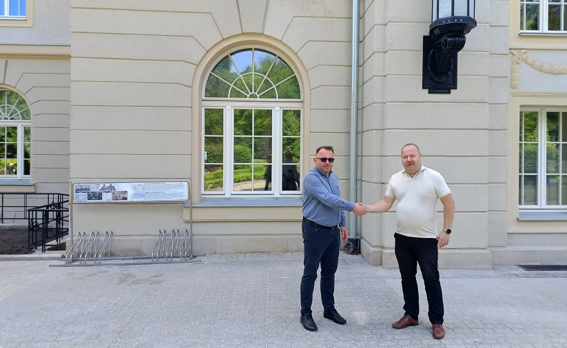 Prezes uzdrowiska i zastępca burmistrza ściskają sobie dłonie, w tle budynek