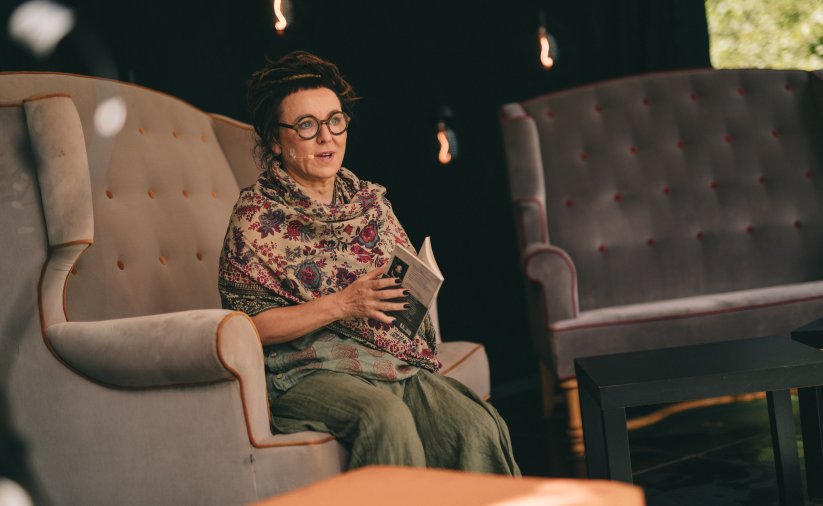 Olga Tokarczuk siedząca w duzym fotelu z książką w rękach