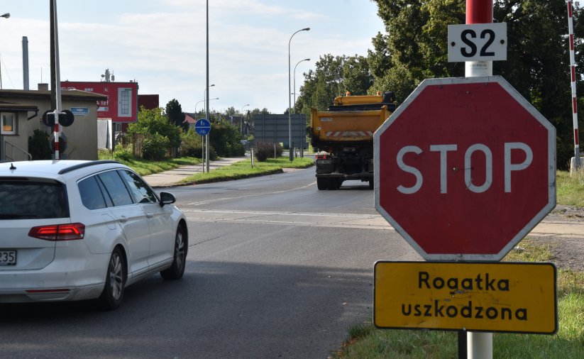 Biały samochód przed przejzadem kolejowy, po prawej znak "Stop"