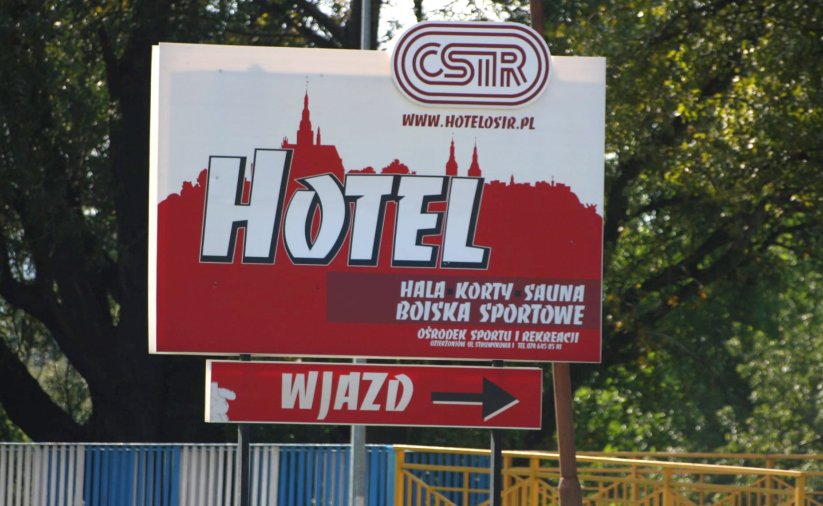 Duży baner przy drodze dojazdowej do ośrodka sportu z napisem hotel