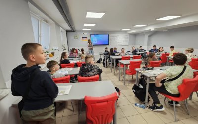 Klasa szkolna, białe ławki, czerwone krzesła, na ścianie tablica multimedialna
