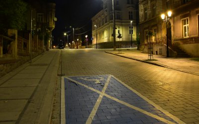 Noc, pomalowane na niebiesko miejsce postojowe, droga dookoła kamienice