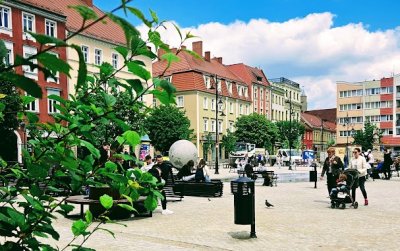 Rynek wyłożony kamienną kstką, po lewej zieleń, w tle kamienice