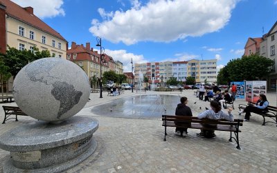 Duży kamienny globus ustawiony w rynku, obok ławka, na drugim planie fontanna