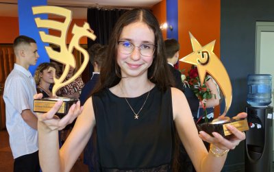 Uśmiechnięta uczennica trzymająca dwie statuetki