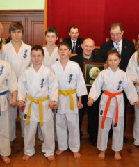 Grupa karateków w białych strojach na zdjęciu z burmistrzem i przewodniczącym rady