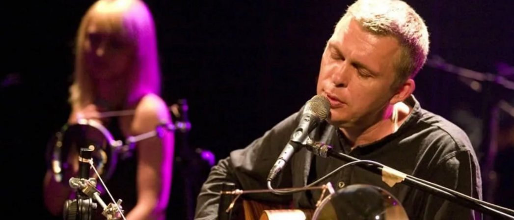 Wokalista przy mikrofonie z gitarą, w tle kobieta