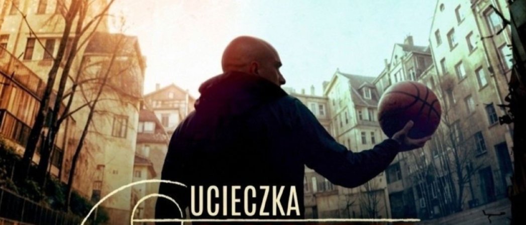 Chłopak w bluzie z kapturem stojący tyłem, w wyciągniętej ręce trzyma piłkę do kosza