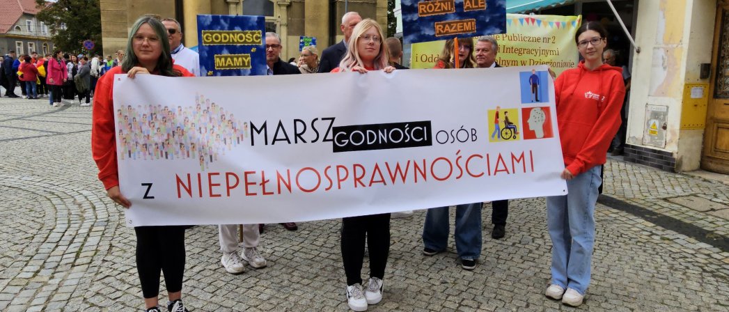 Trzy dziewczyny trzymające baner z napisem "Marsz osób z niepełnosprawnościami"