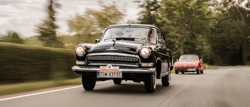 Czarne, zabytkowe auto "Wołga" jadące asfaltowa drogą