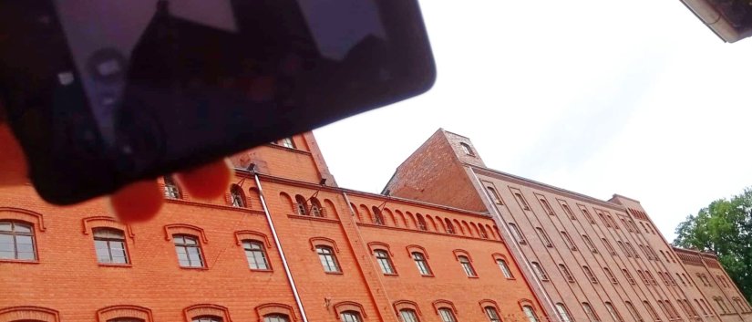 ogromny budynek z czerwonej cegły, przed nim ręka trzymająca telefon