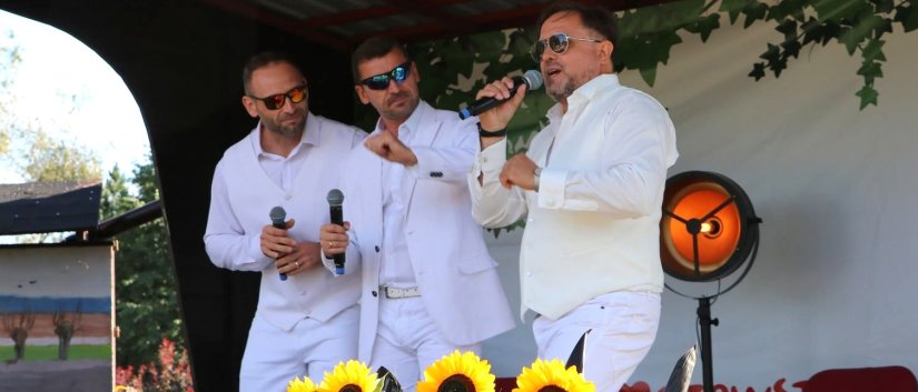 Trzech mężaczyzn w białych strojach śpiewa na niewielkiej scenie